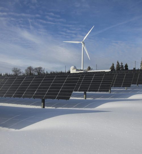 Solar panels and wind turbine in a snowy landscape, showcasing renewable energy sources.